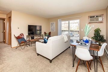 Ankeny apartment for rent - A living room with a white couch, a white chair, a white dining table and chairs, a television, and a potted plant.