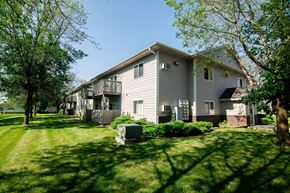 Ankeny apartment for rent - A house with a grey siding and a balcony is surrounded by green grass and trees at Peach Tree Apartments, Ankeny, IA
