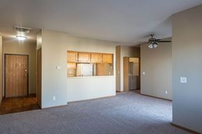 Waukee apartment for rent - an empty living room with a kitchen and a ceiling fan at Sunrise Meadows, Waukee, IA