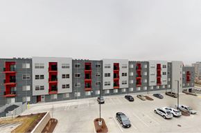Des Moines apartment for rent - A large grey building with red accents and a parking lot in front at Vue Apartments, Des Moines