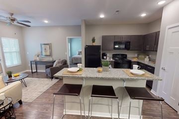 Altoona apartment for rent - A kitchen with a black fridge and microwave, a dining table with chairs, and a living room with a couch and a coffee table.