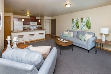 Des Moines apartment for rent - A living room with a grey couch and a kitchen in the background.