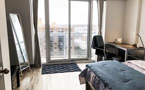Waterloo apartment for rent - A bedroom with a large bed, desk, and a view of the city through the window.