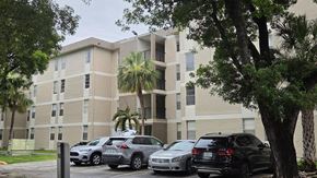 Hialeah apartment for rent - A parking lot with cars and a building with palm trees in front.