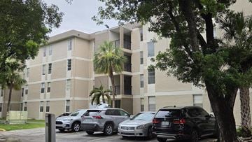 Hialeah apartment for rent - A parking lot with cars and a building with palm trees in front.