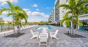 Miami apartment for rent - a pool with chairs and palm trees next to a building