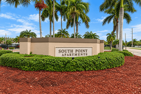 Miami apartment for rent - A sign for South Point Apartments is surrounded by a hedge and palm trees.