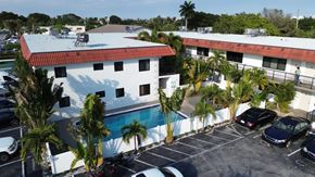 Lighthouse Point apartment for rent - A white building with a red roof is surrounded by a parking lot.