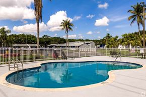 Riviera Beach apartment for rent - A round blue swimming pool surrounded by a fence with palm trees in the background.