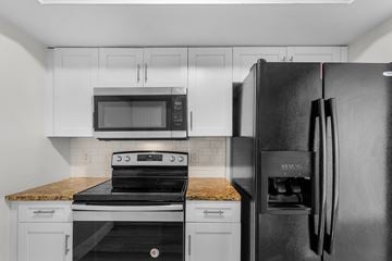 Fort Myers apartment for rent - A black refrigerator stands in a kitchen with a stove and microwave above it.