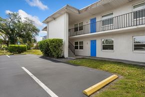 Fort Myers apartment for rent - A white building with a blue door and a yellow barrier in front.