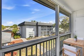 Fort Myers apartment for rent - A balcony with a table and chairs overlooks a building and a garden.
