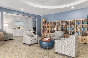 Kent apartment for rent - A living room with a grey patterned armchair, a blue ottoman, a wooden bookshelf, and a painting on the wall.