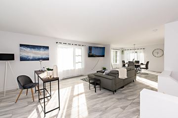 Val D'or apartment for rent - A living room with a grey sofa, a black chair, and a painting on the wall.
