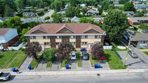 Gatineau apartment for rent - A large brick building with a brown roof is surrounded by a grassy area and a parking lot with several cars.