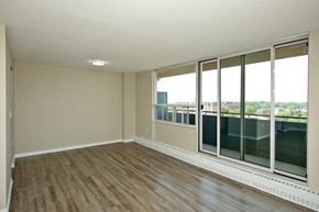 Oshawa apartment for rent - A room with wooden floors and a large window overlooking a cityscape.