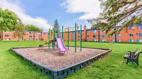 Oakdale apartment for rent - A playground with a slide, swings, and a seesaw in front of a building.