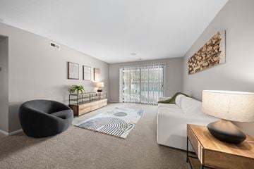 Clinton Township apartment for rent - A living room with a white couch, a black chair, and a wooden side table with a lamp.