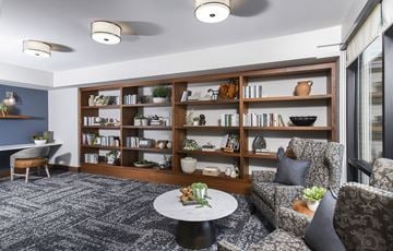 Goodyear apartment for rent - A living room with a grey carpet and a bookshelf filled with books and decorative items.