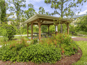 Lehigh Acres apartment for rent - A wooden gazebo is surrounded by green plants and trees. at Heron Pond 55+ Apartments, Lehigh Acres, FL