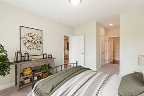 Greenville apartment for rent - A bedroom with a bed, a table with a plant, and a painting on the wall. at Avery Landing Apartments, Greenville, 29605