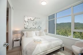 Coquitlam apartment for rent - A bedroom with a large bed and a view of the forest outside the window.