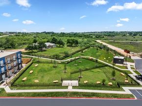 Jarrell apartment for rent - A large grassy area with trees and a fence in the foreground and a building to the left.