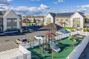East Patchogue apartment for rent - A fenced playground is surrounded by parking and two buildings