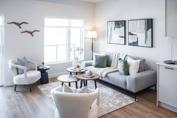 Welland apartment for rent - A living room with a grey couch, a white chair, and a table with a vase on it.