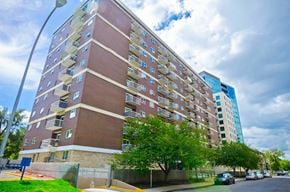 Calgary apartment for rent - A tall apartment building with a blue sky and clouds in the background.