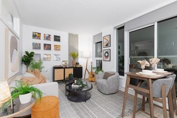 Calgary apartment for rent - A living room with a grey couch, a coffee table, a guitar, and a dining table with chairs.
