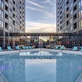Calgary apartment for rent - A large indoor swimming pool with lounge chairs is surrounded by two tall buildings.