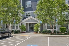 Merrimack apartment for rent - A black car is parked in a parking lot in front of a grey building.
