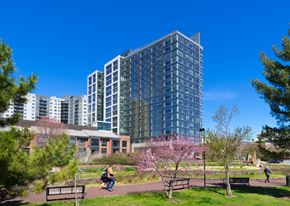 Philadelphia apartment for rent - A modern glass building is surrounded by trees and people are walking around.