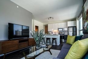Clayton apartment for rent - A modern living room with a television, a glass coffee table, and a kitchen in the background at Two Twelve Clayton Apartments, Clayton, MO