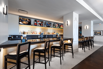 A bar with black chairs and a counter with bottles on it.