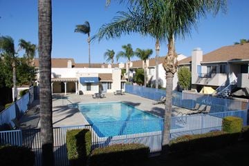 Perris apartment for rent - A pool surrounded by palm trees and a fence.