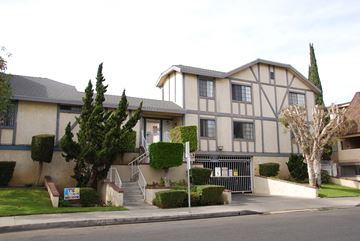 Hawthorne apartment for rent - A building with a grey and white facade is surrounded by greenery and a metal gate.