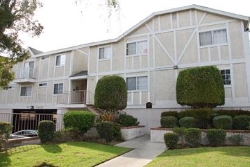 Hawthorne apartment for rent - A white building with a balcony and a green bush in front.