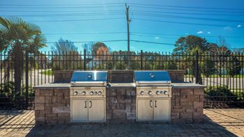Two gas bbqs in front of a stone wall with a fence