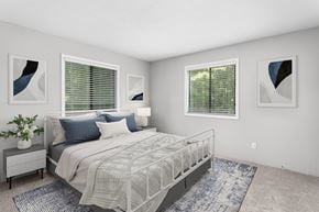 Greensboro apartment for rent - A bedroom with a large bed, a nightstand with a plant, and two framed artworks on the wall.
