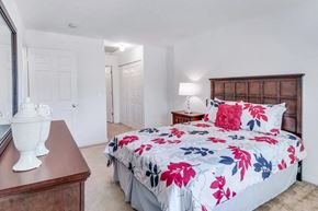 Henrico apartment for rent - A bed with a floral print is in the center of a bedroom with a wooden dresser and a white vase on top.