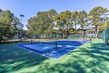 A blue and green tennis court with trees in the background