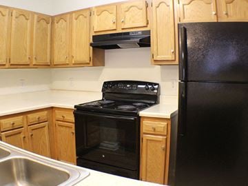 Greensboro apartment for rent - A black stove and refrigerator in a kitchen with wooden cabinets.