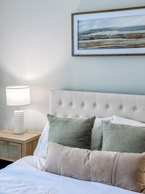Hampton apartment for rent - A bed with a white headboard and a painting above it.