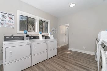 A laundry room with two washers and dryers and a door to a hallway
