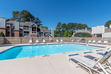 Raleigh apartment for rent - A swimming pool surrounded by lounge chairs and buildings in the background.