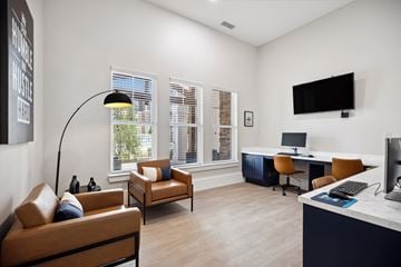Charlotte apartment for rent - A living room with a brown leather couch, a desk with a computer, and a television mounted on the wall.