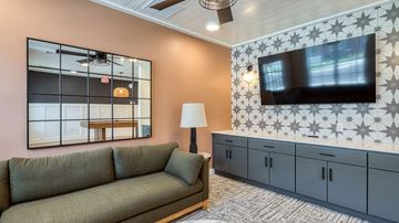 Glen Allen apartment for rent - A living room with a grey sofa, a large mirror, and a television mounted on the wall.