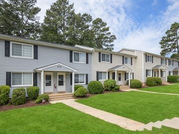 Raleigh apartment for rent - A row of houses with green lawns and trees in the background.